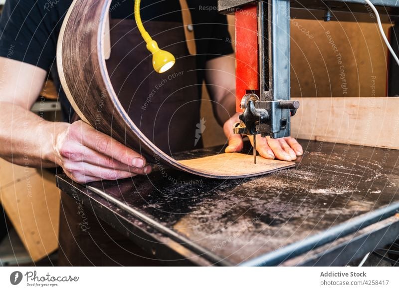 Anonymer Geigenbauer schneidet Gitarrenkorpus auf Bandsäge im Arbeitsraum Zupfinstrumentenmacher machen geschnitten Handwerk Holzarbeiten Werkstatt Mann