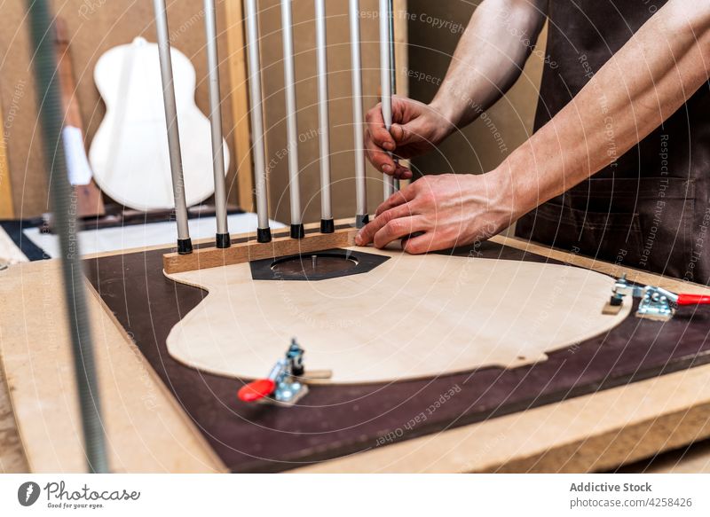Handwerker bei der Montage von Metallstäben beim Bau einer Gitarre im Arbeitsraum Zupfinstrumentenmacher bauen kleben installieren professionell Genauigkeit
