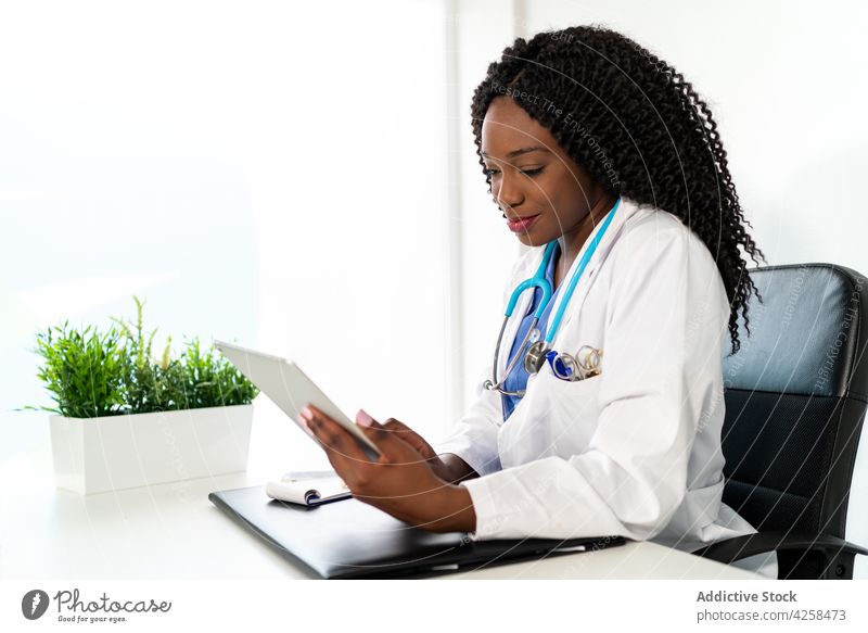 Lächelnde schwarze Frau in medizinischer Uniform, die ein Tablet im Krankenhaus benutzt Arzt benutzend Klinik Tablette Medizin Arbeit Gesundheitswesen