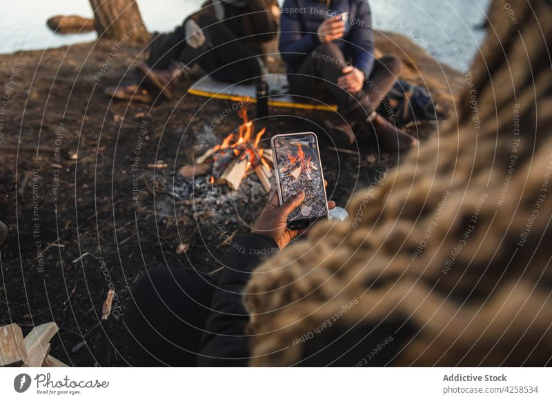 Anonyme schwarze Frau fotografiert Feuer beim Camping mit Freunden Menschen fotografieren Smartphone Wohnmobil Freudenfeuer Reisender Zusammensein