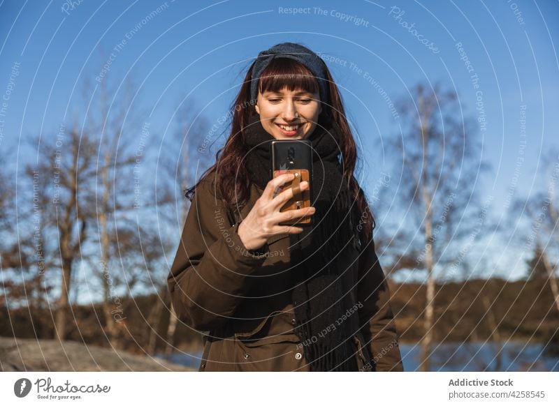 Lächelnde Frau beim Fotografieren mit dem Smartphone benutzend positiv fotografieren Gedächtnis Natur Herbst Anschluss heiter froh Optimist lässig Funktelefon