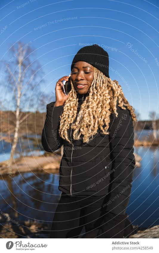Schwarze Frau steht am Ufer in der Nähe eines Teiches Smartphone reden benutzend Kommunizieren sprechen Fluss Küste Natur zuhören Mobile Apparatur Lächeln