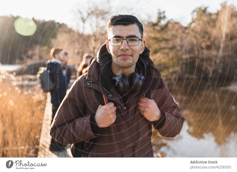 Lächelnder ethnischer Mann schaut in die Kamera in der Nähe eines Sees im Herbstwald Natur Park Wanderung Reisender Freund positiv Zusammensein Freundschaft