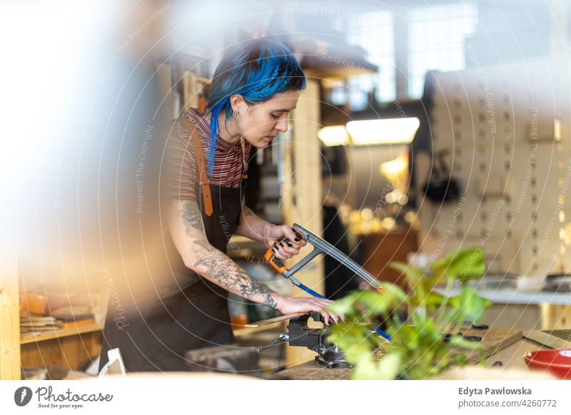 Frau mit Handsäge in ihrer Werkstatt diy Hipster farbenfroh Behaarung Tattoos Besitzer Beruf Dienst Kleinunternehmen Mitarbeiter arbeiten Techniker Arbeitsplatz
