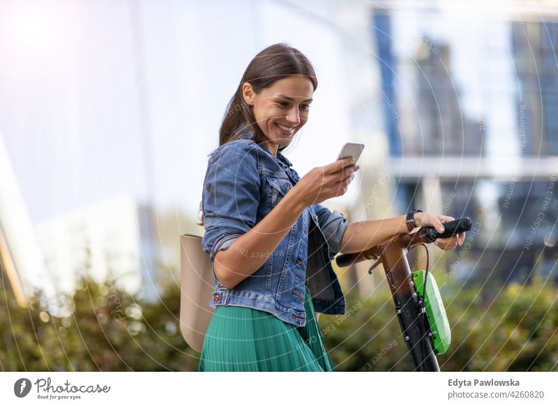 Elektroroller vom Smartphone aus aktivieren urban Straße Großstadt Menschen Frau junger Erwachsener lässig attraktiv Glück Kaukasier genießend eine Person schön