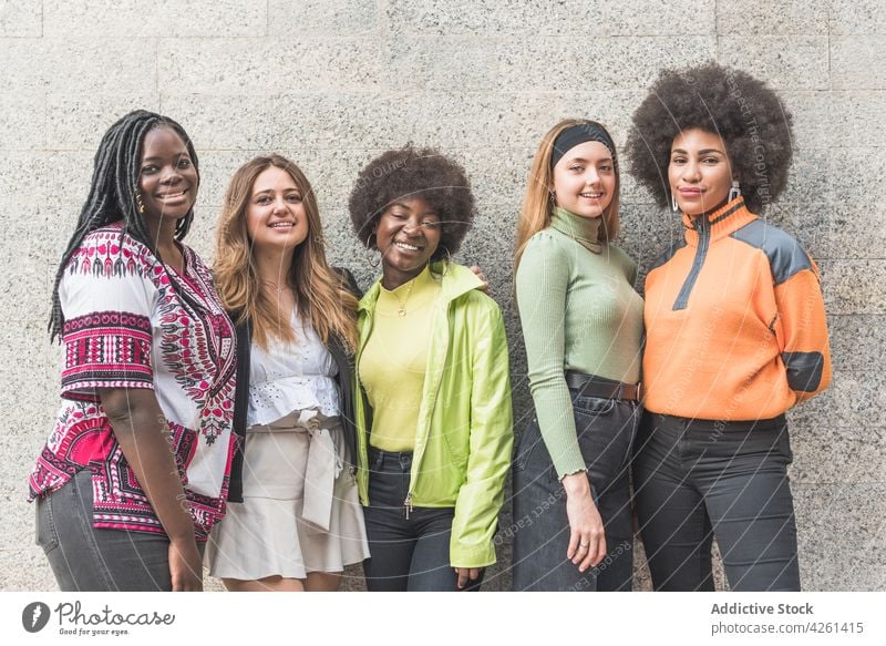 Selbstbewusste multirassische Freundinnen in Freizeitkleidung an der Wand selbstsicher Glück Streetstyle Mode Lächeln Individualität eitel Freundschaft feminin