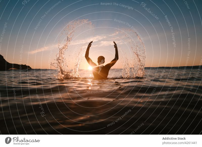 Unbekannter Sportler im Meer mit spritzendem Wasser im Sonnenschein Arme hochgezogen platschen Natur Meereslandschaft Himmel wellig Sonnenuntergang Mann Athlet