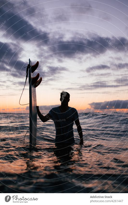 Anonymer Surfer mit Surfbrett im Meer bei Sonnenuntergang Sportler Silhouette Natur Meereslandschaft wolkig Himmel Mann Gerät professionell Atmosphäre Air