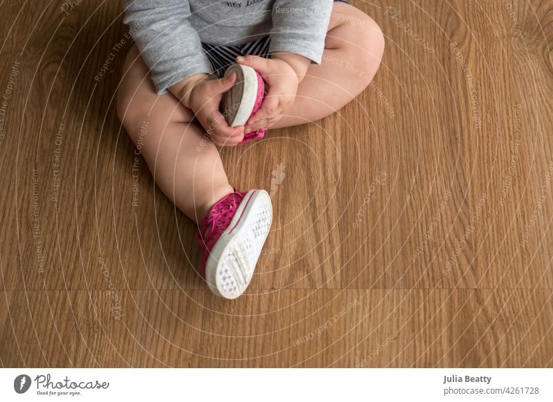 Junge Kleinkind Baby hält Fuß mit rosa und weißen Schuh auf; Erkundung erste Paar Schuhe oddler erste Schuhe sitzen Halt sitzend Füße zusammen Körperhaltung