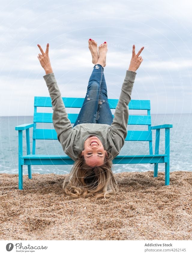 Lächelnde Frau, die sich auf einer Bank am Meer amüsiert zwei Finger Spaß haben Beine gekreuzt heiter Wochenende Frieden angehobene Beine Meeresufer Himmel