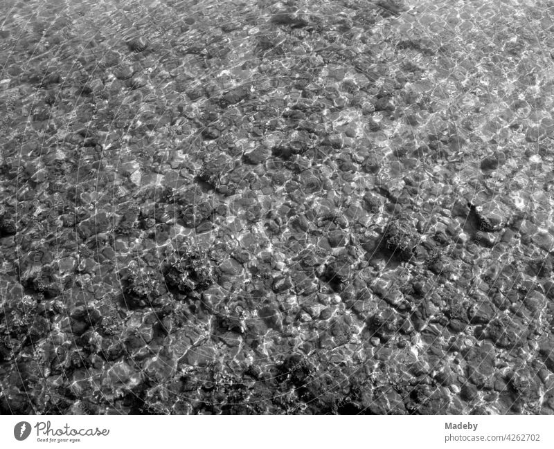 Seichtes Wasser mit Steinen am Strand in Alacati bei Cesme in der Provinz Izmir am Ägäischen Meer in der Türkei, fotografiert in klassischem Schwarzweiß
