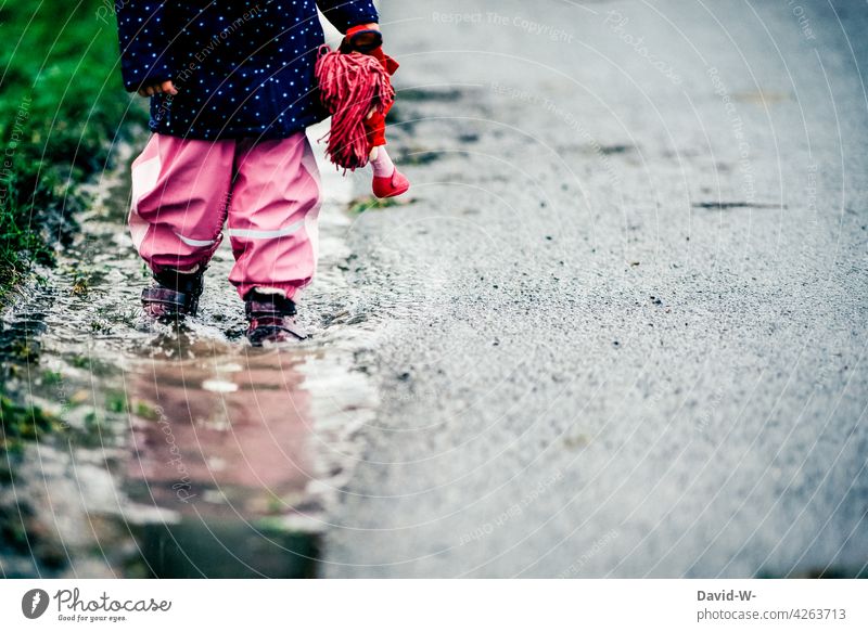 Kind am Straßenrand Straßenverkehr Gefahr Pfütze Regenwetter Puppe schlechtes Wetter nass Herbst Achtung Risiko