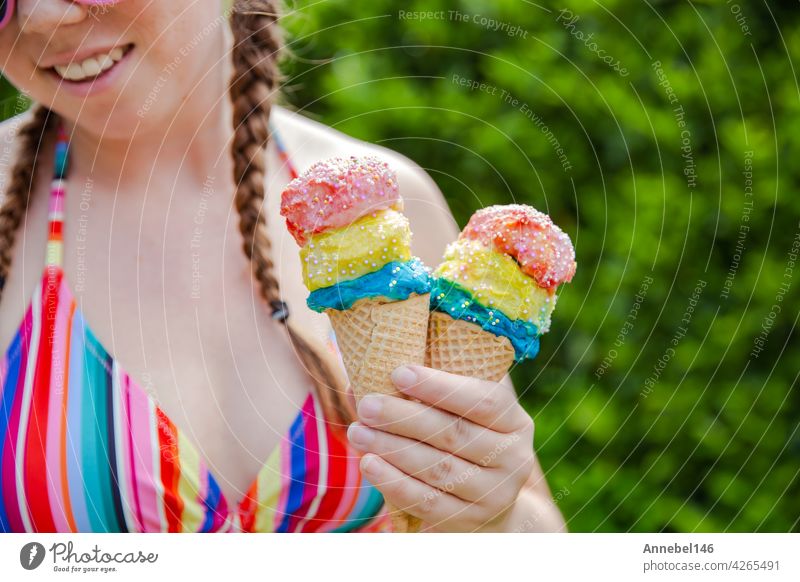 Schönes Mädchen hält zwei bunte Eis mit Streuseln tragen einen Regenbogen farbigen Badeanzug im Sommer, rosa Sonnenbrille und Zöpfe glücklichen Urlaub, Urlaub Konzept