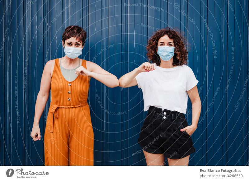 zwei kaukasischen Frauen im Freien tragen Gesichtsmaske Gruß mit Ellbogen. Pandemie während Corona-Virus sozialen Abstand Konzept. COVID Kaukasier vermeiden