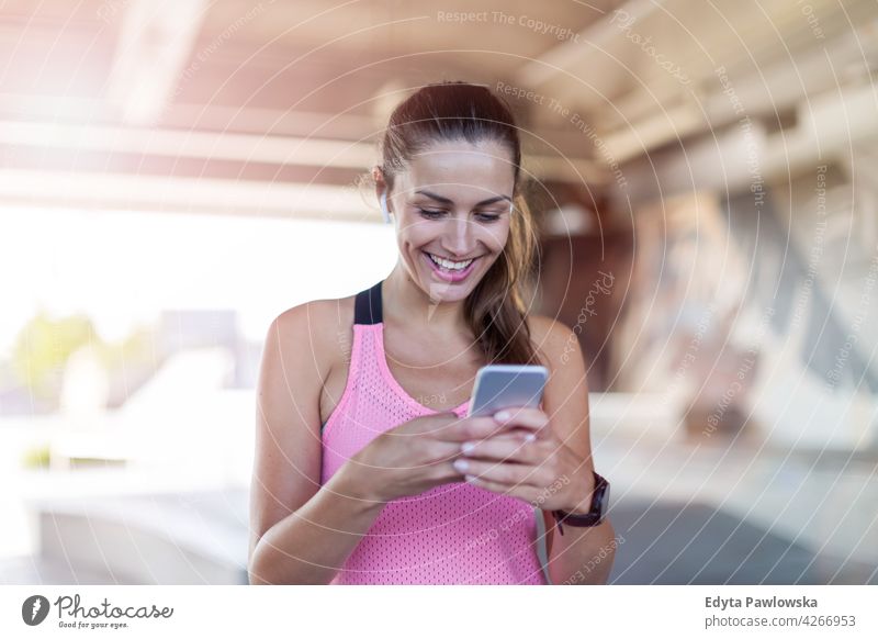 Junge Frau überprüft ihr Smartphone nach dem Training Energie trainiert. Fitness Sport Aktivität Vitalität Körper Turnkleidung anstrengen beweglich Flexibilität