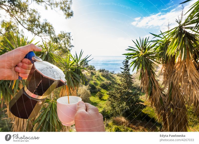 Hand Pouring Kaffee in Tasse gegen Meer, blauer Himmel und exotische Bäume Handfläche tropisch Insel schön Paradies Palme Schönheit grün Garten Kaffeetasse