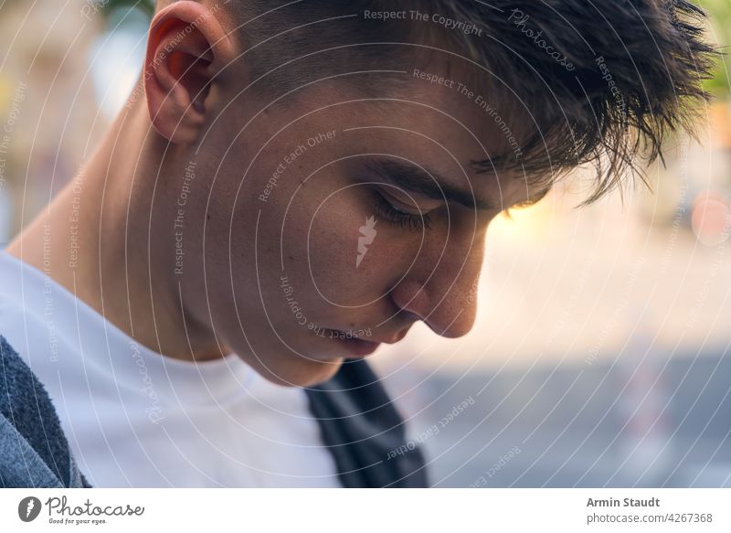 Nahaufnahme eines nachdenklich dreinblickenden Teenagers Porträt jung Mann besinnlich sensibel Blick ruhig Schatten Sonne hintergrundbeleuchtet Sonnenlicht