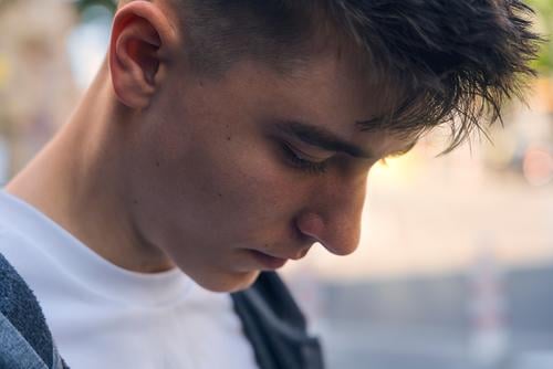 Nahaufnahme eines nachdenklich dreinblickenden Teenagers Porträt jung Mann besinnlich sensibel Blick ruhig Schatten Sonne hintergrundbeleuchtet Sonnenlicht