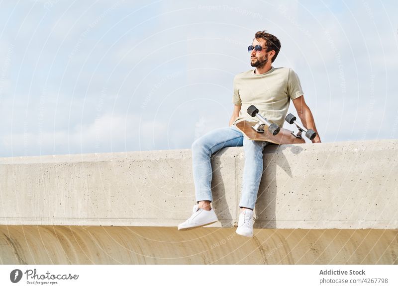 Cooler Mann mit Skateboard, der sich am Rand einer Böschung ausruht MEER Kälte Stauanlage Ufer Hafengebiet maskulin sorgenfrei sich[Akk] entspannen männlich