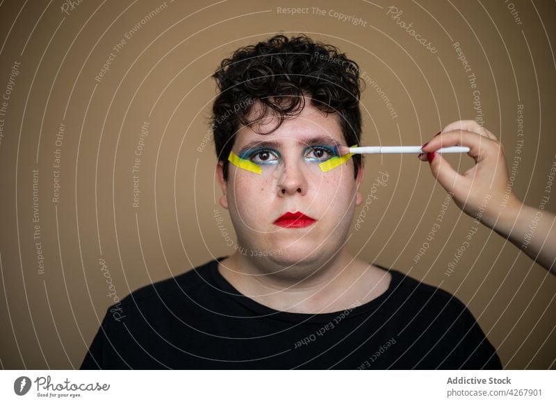 Visagist trägt hellen Lidschatten auf das Gesicht eines androgynen Mannes auf visagiste Bürste bewerben Make-up Schönheit queer männlich Stylist alternativ