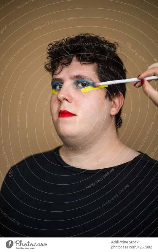 Visagist trägt hellen Lidschatten auf das Gesicht eines androgynen Mannes auf visagiste Bürste bewerben Make-up Schönheit queer männlich Stylist alternativ