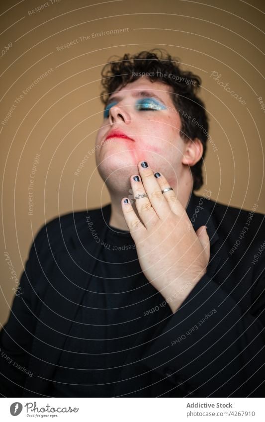 Verführerischer Mann mit leuchtendem Make-up, der seine Lippen berührt sinnlich queer Transgender verführerisch provokant exzentrisch ungewöhnlich Geschlecht