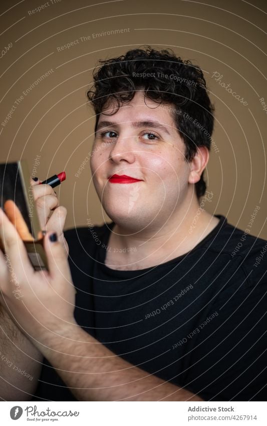 Übergewichtiger Mann mit Spiegel, der roten Lippenstift aufträgt bewerben Kosmetik Kosmetologie Transgender Make-up Gesicht androgyn männlich queer extravagant