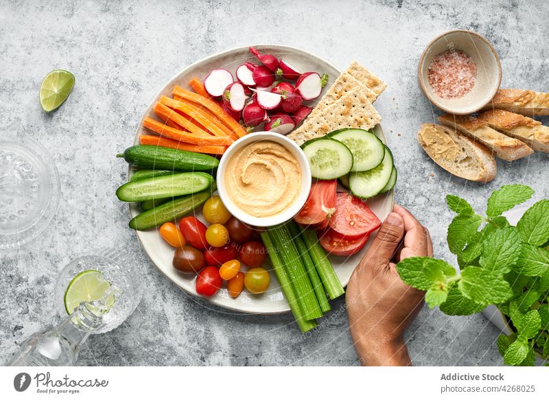 Gemüseteller mit gesundem, frischem Gemüse und Hummus, serviert auf dem Tisch neben Brot Person gesunde Ernährung Salatgurke Tomate Möhre Rettich Spinat