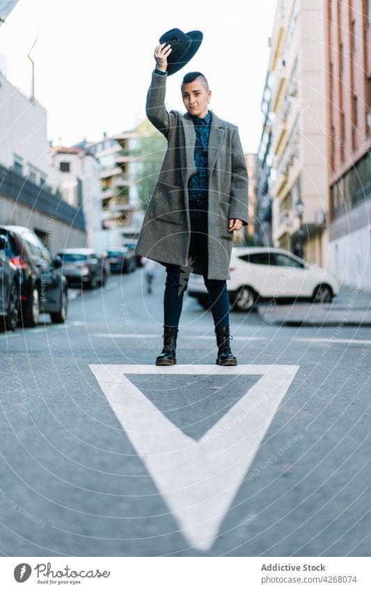 Androgyne Person mit Hut auf städtischer Straße androgyn Mode Stil Arm angehoben lgbtq Großstadt Lifestyle zeigen Pfeil transsexuell Individualität Identität
