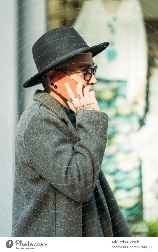 Queer spricht auf Smartphone auf Straße Hintergrund queer reden Stil Mode Sonnenbrille Individualität Geschlecht benutzend Apparatur Gerät modern Mantel lgbt