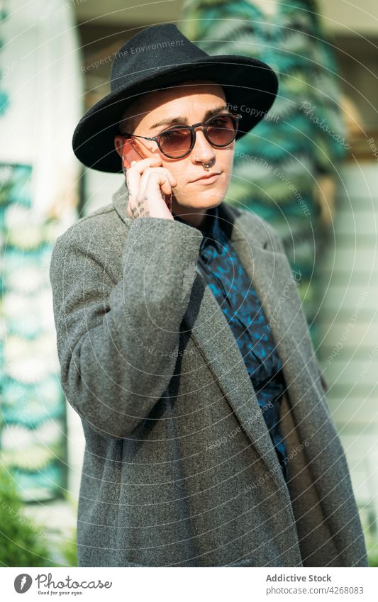 Queer spricht auf Smartphone auf Straße Hintergrund queer reden Stil Mode Sonnenbrille Individualität Geschlecht benutzend Apparatur Gerät modern Mantel lgbt