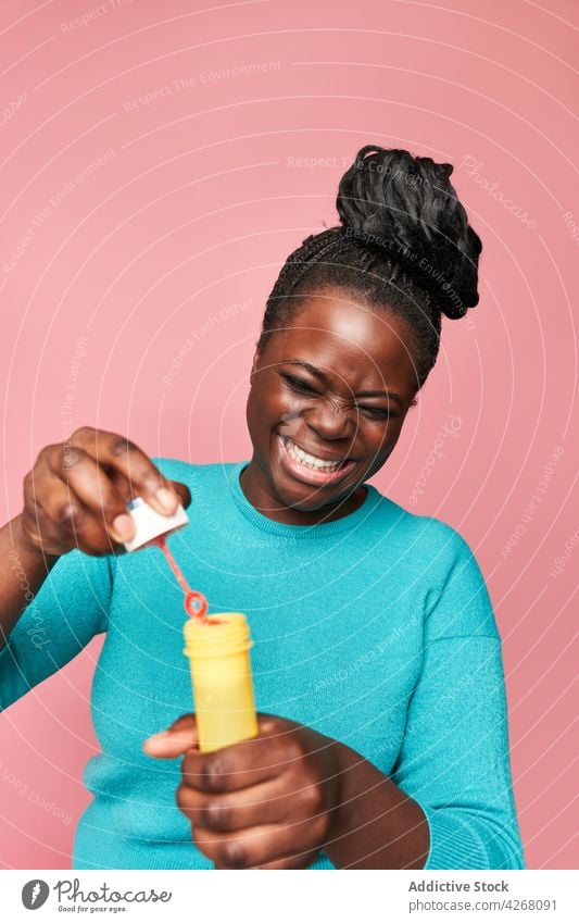 Fröhliche schwarze Frau, die im Studio Seifenblasen bläst Schaumblase ethnisch Schlag freudig Afroamerikaner Glück farbenfroh lebhaft spielerisch Spielzeug
