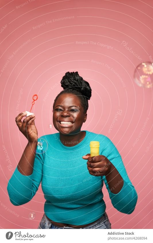 Fröhliche schwarze Frau, die im Studio Seifenblasen bläst Schaumblase ethnisch Schlag freudig Afroamerikaner Glück farbenfroh lebhaft spielerisch Spielzeug