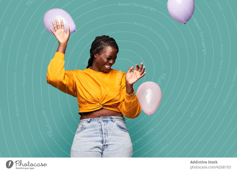 Fröhliche schwarze Frau spielt mit Luftballons im Studio aufgeregt Glück freudig spielerisch spielen Lachen Augen geschlossen lebhaft Spaß haben Stil farbenfroh