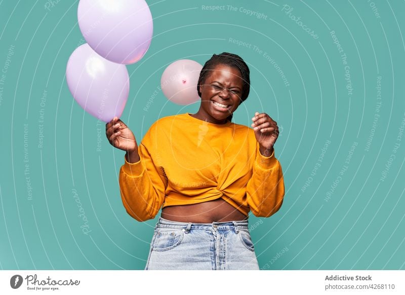 Fröhliche schwarze Frau spielt mit Luftballons im Studio aufgeregt Glück freudig spielerisch spielen Lachen Augen geschlossen lebhaft Spaß haben Stil farbenfroh