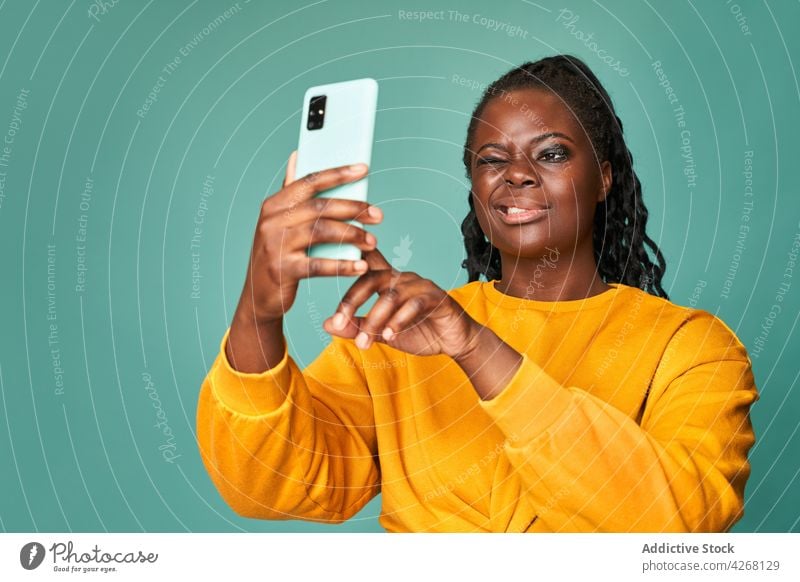 Zufriedene schwarze Frau, die zwinkert und ein Selfie mit ihrem Smartphone macht Zwinkern fotografieren Glück heiter Fotografie Grimasse lebhaft