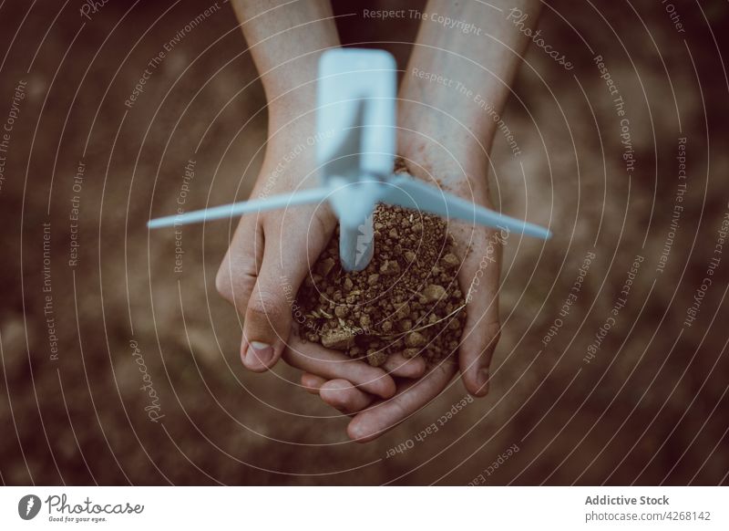Person mit einer Handvoll Erde und einer Miniaturmühle Boden Windmühle Ökologie alternativ Energie Konzept Erneuerung Kraft Industrie Turbine Schonung Werkzeug