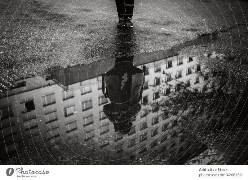 Person in Oberbekleidung steht auf der Straße und spiegelt sich in einer Pfütze Reflexion & Spiegelung nass Fassade Asphalt Gebäude trist Regen bedeckt Weg