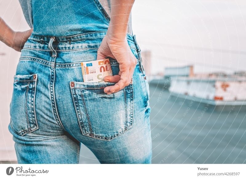 Eine Frauenhand holt Euroscheine aus der Gesäßtasche ihrer Jeans. Das Konzept der Finanzen, Ersparnisse, finanzielle Ausgaben. Nahaufnahme. Kopierraum Hand