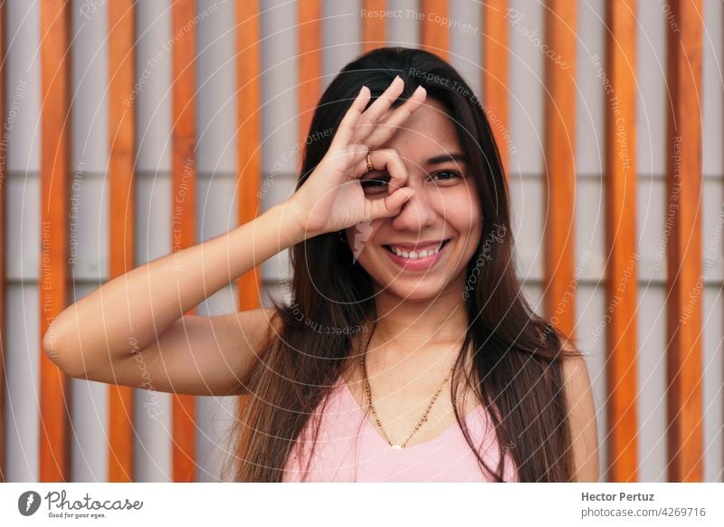 Attraktive junge Frau macht das richtige Zeichen und bedeckt ihr Auge, drückt Emotion, Modell posiert im Freien Porträt Erwachsener lässig lateinamerikanisch