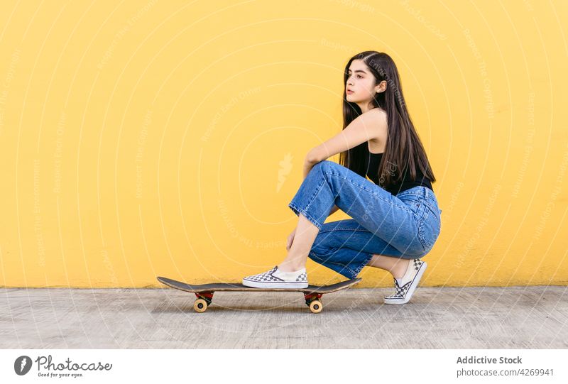 Skater hockt auf Skateboard auf gelbem Hintergrund Skateboarderin Sport verträumt lässig Stil tausendjährig charmant Laufsteg Teenager Outfit wehmütig