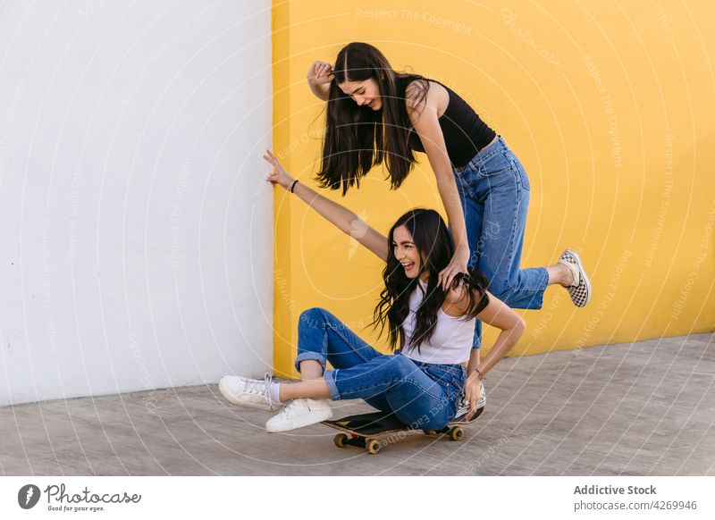 Glückliche Schwestern haben Spaß beim Skateboardfahren auf dem Bürgersteig Mitfahrgelegenheit Spaß haben Sport Freizeit Erholung heiter Beine gekreuzt