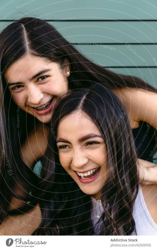 Lächelnde Schwestern mit langen Haaren auf grünem Hintergrund herzlich freundlich angenehm charmant feminin sich auf die Hand lehnen Art Porträt Teenager