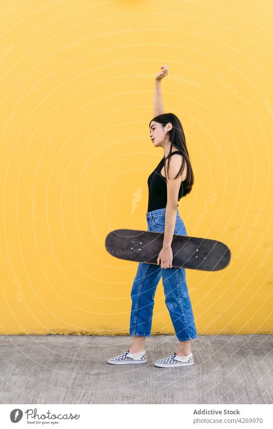 Skateboarder in Freizeitkleidung auf dem Bürgersteig auf gelbem Hintergrund Skater Arm angehoben cool Zeitgenosse Generation freie Zeit Lifestyle Teenager