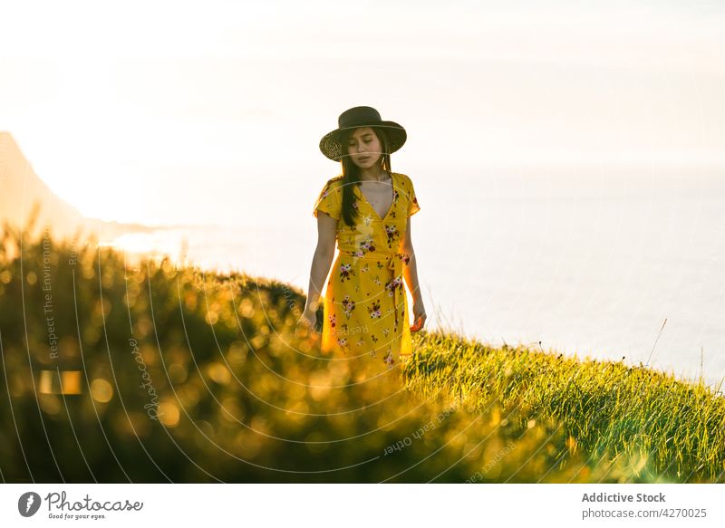 Junge Frau steht auf einem Rasenstück Sonnenkleid Landschaft Natur verträumt Grasland Wiese grasbewachsen jung Feld Hut Vorschein Gelassenheit Anmut feminin