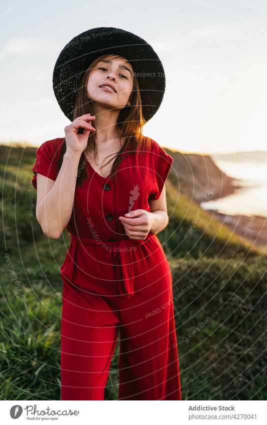 Junge Frau steht auf einem Rasenstück Sonnenkleid Landschaft Natur verträumt rot Grasland Wiese grasbewachsen jung Feld Hut Vorschein Gelassenheit Anmut feminin