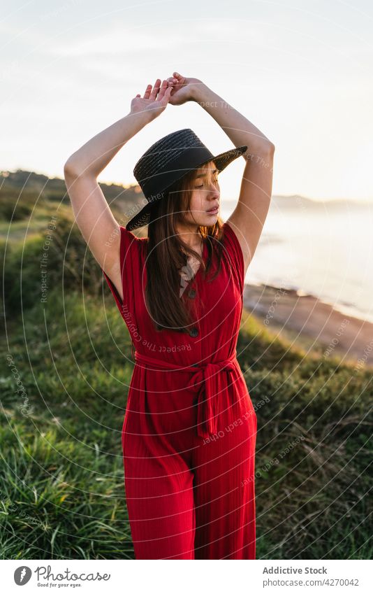 Junge Frau steht auf einem Rasenstück Sonnenkleid Landschaft Natur verträumt rot Grasland Wiese grasbewachsen jung Feld Hut Vorschein Gelassenheit Anmut feminin