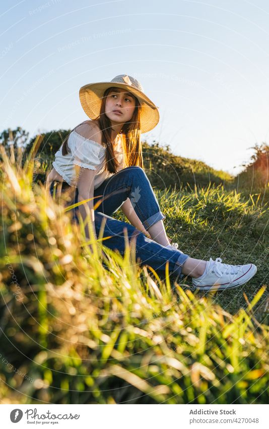 Junge Frau auf einer Wiese in sonniger Landschaft sitzend Rasen verträumt friedlich Sommer ruhen Natur Gelassenheit grasbewachsen trendy Vorschein ruhig