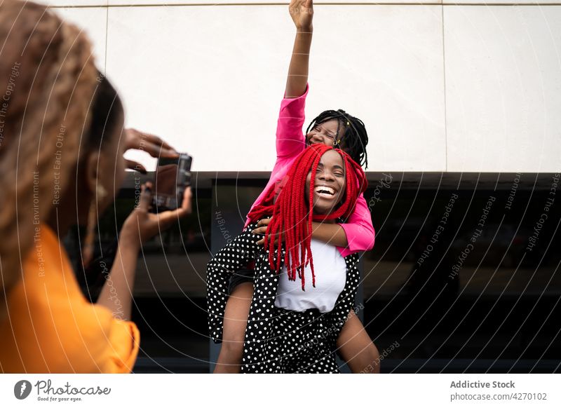 Schwarze Frau fotografiert ihre Freunde beim Huckepackfahren Frauen fotografieren Fotoapparat Spaß haben Lachen genießen heiter Zusammensein Freundin