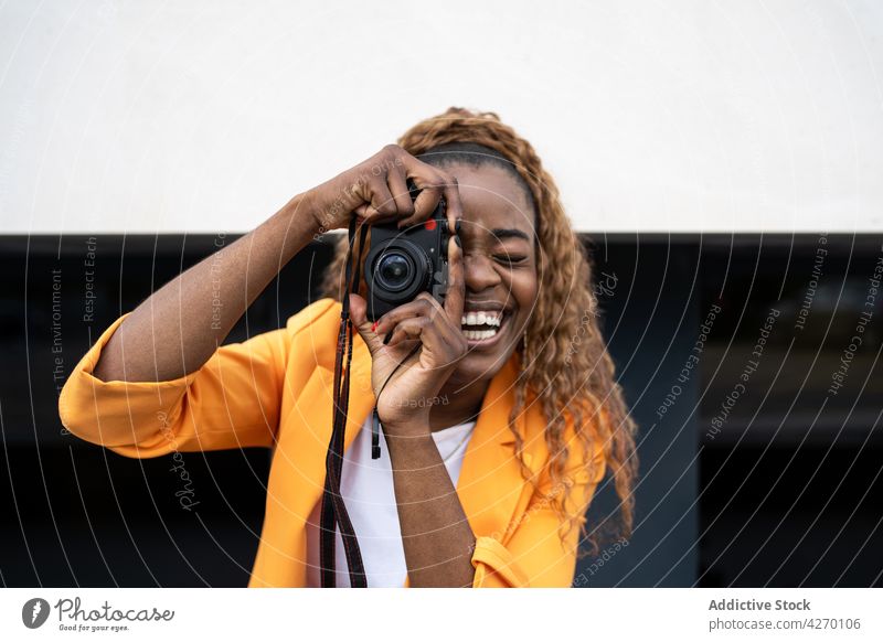 Schwarze fröhliche Frau, die ein Foto mit der Kamera macht Lachen genießen Freizeit Glück fotografieren Fotoapparat Spaß einfangen Hobby Optimist heiter
